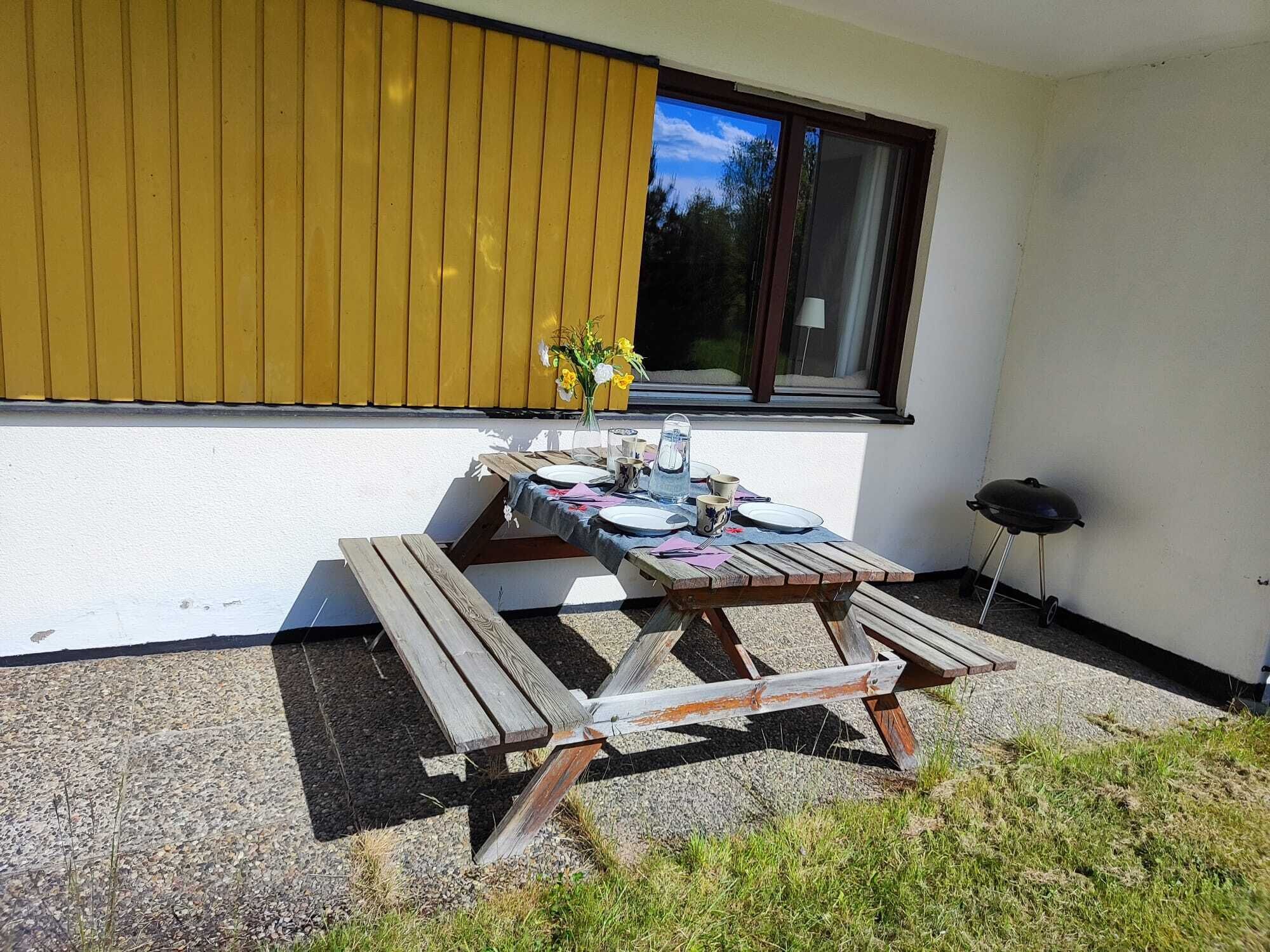 A patio with a table set for four, a grill, and a window with blinds.