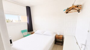 Een slaapkamer met een bed, een stoel, een nachtkastje en een kledingrek.