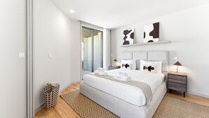 Ein modernes Hotelzimmer mit einem großen Bett, einem Nachttisch, einer Lampe und abstrakter Wandkunst.