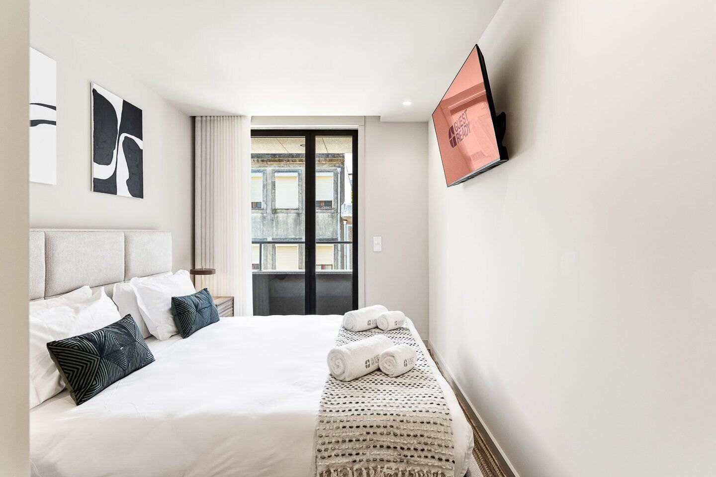 Quarto de hotel com cama, televisão, janela com vista e porta para uma varanda.