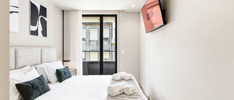Quarto de hotel com cama, televisão, janela com vista e porta para uma varanda.