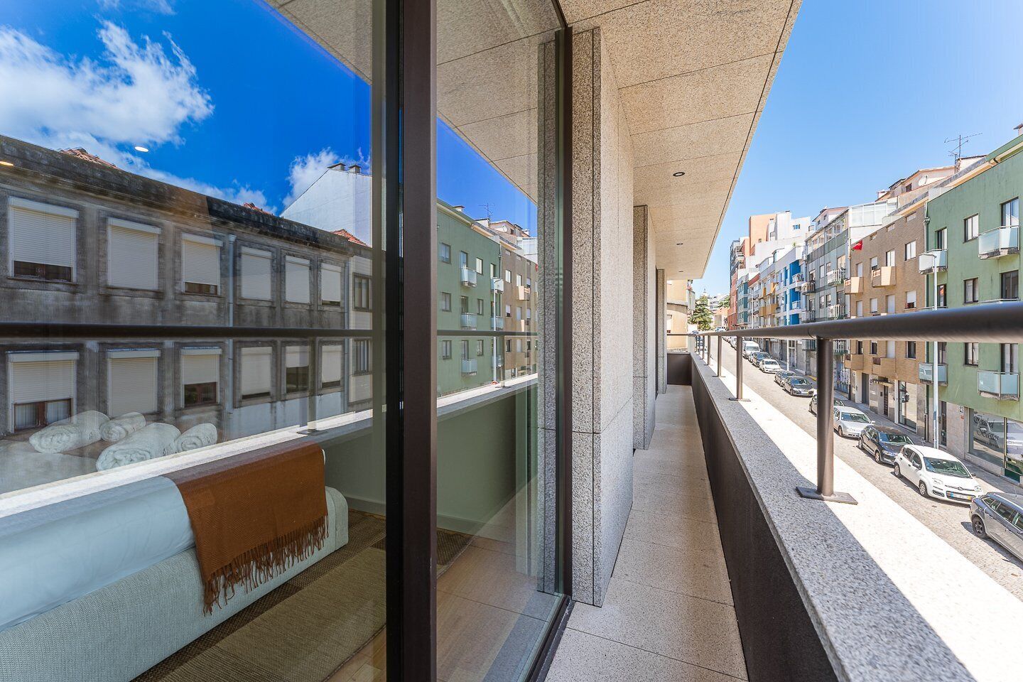 A balcony with a view of a street, a window with a towel, and a cushion.