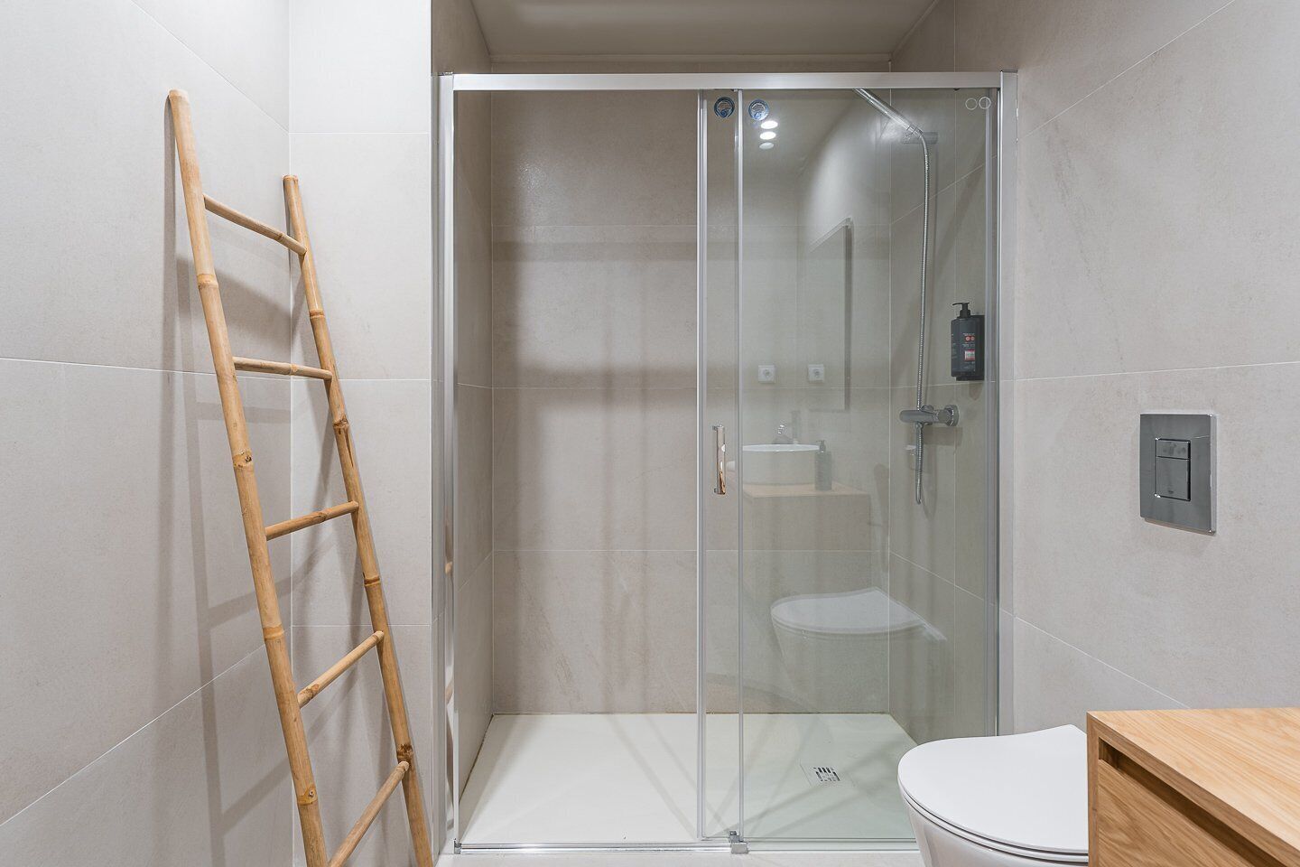 Un baño moderno con ducha de vidrio, una escalera de madera y un inodoro blanco.