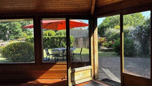 Et værelse med træpaneler og en stor skydedør, der fører ud til en udendørs terrasse med et bord, stole og en rød parasol.