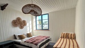 Et soveværelse med seng, bænk, et vindue og en hængende lampe.