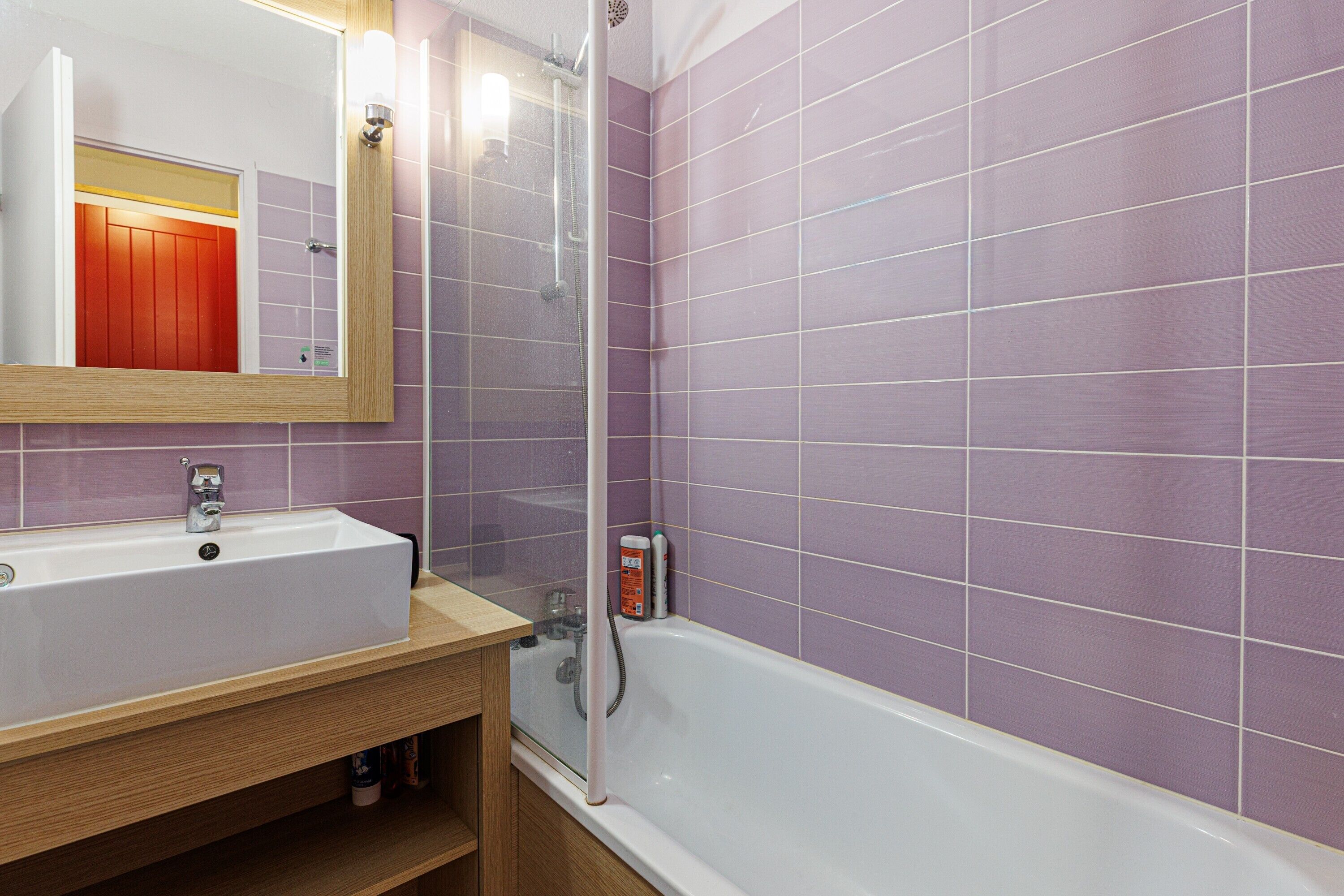 A bathroom with a sink, mirror, shower, and purple tiled walls.