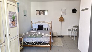 Een slaapkamer met een bed, nachtkastje, lamp, stoel en een deur met een plant.