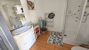 Een badkamer met houten vloer, een witte wastafel, een spiegel, een douche en een handdoekhouder.