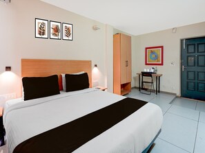 Ein Hotelzimmer mit Bett, Nachttischlampen, Schreibtisch mit Stuhl, Kleiderschrank und gerahmten Bildern an der Wand.