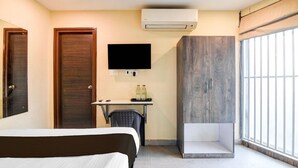 Habitación de hotel con cama, escritorio con silla, televisor en la pared, equipo de aire acondicionado y un ventanal con vistas.