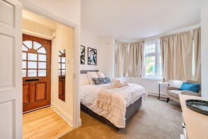 Ein Schlafzimmer mit einem Bett, einem Nachttisch, einem Fenster mit Vorhängen und einer Tür mit Holzpaneel.