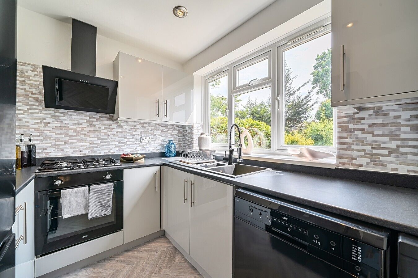 A modern kitchen with a built-in microwave, stove, and dishwasher, featuring a herringbone tile backsplash and large windows.