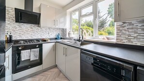 Et moderne køkken med indbygget mikroovn, komfur og opvaskemaskine, med et backsplash af fiskebensmønstret fliser og store vinduer.
