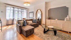 En moderne stue med en hjørnesofa, et glasbord og et stort vindue med lette gardiner.