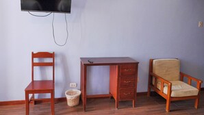 A room with a wooden desk, a chair, a television mounted on the wall, and a small wicker basket on the floor.