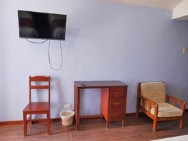 A room with a wooden desk, a chair, a television mounted on the wall, and a small wicker basket on the floor.