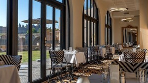 A dining area with large windows, tables, chairs, and a view of a castle.