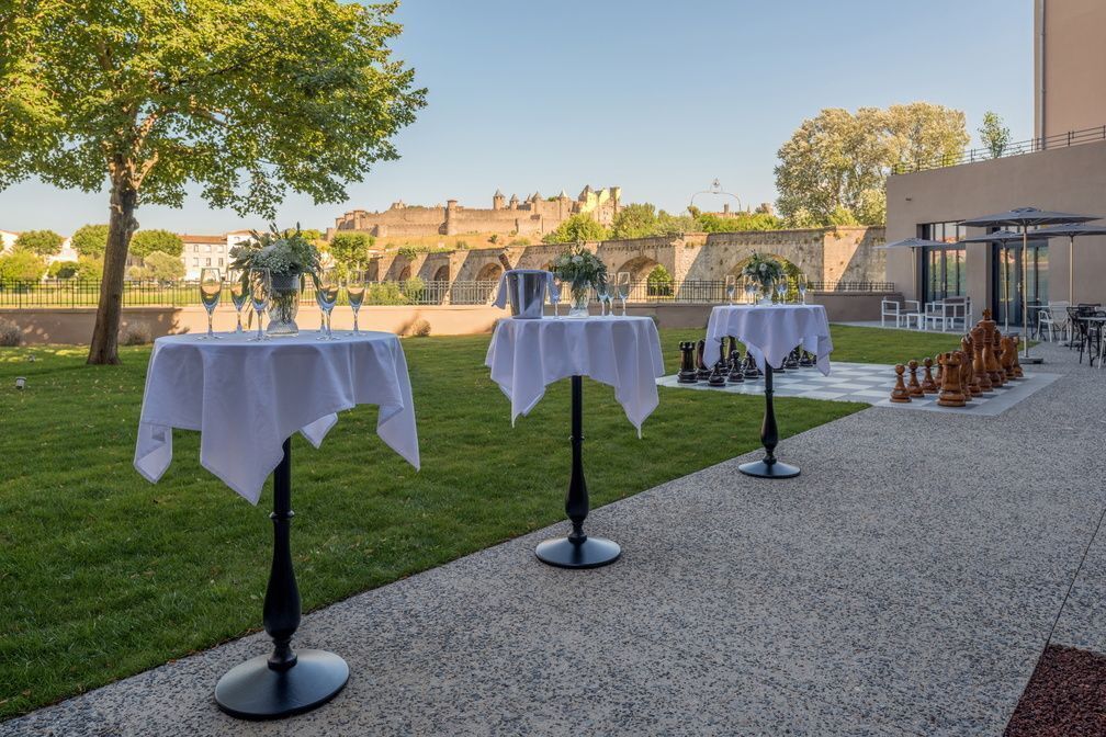 Des tables en plein air recouvertes de nappes blanches, un chemin pavé et, en arrière-plan, une vue sur un bâtiment historique.