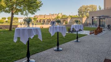 Des tables en plein air recouvertes de nappes blanches, un chemin pavé et, en arrière-plan, une vue sur un bâtiment historique.