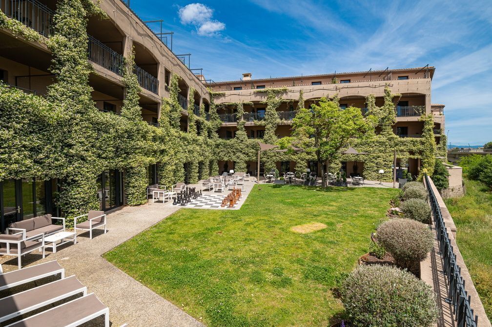 Une cour avec des sièges en plein air, un jeu d’échecs et un bâtiment doté de nombreux balcons.