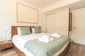 A neatly made bed with white linens and a green throw blanket, a bedside table with a lamp, and a large framed artwork on the wall. - Azure Atlantic Horizon by Atlantic Holiday (Câmara de Lobos)