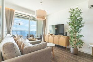 A modern living room with a sofa, a TV, a potted plant, and a view of the sea. - Azure Atlantic Horizon by Atlantic Holiday (Câmara de Lobos)