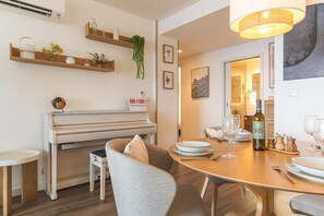 Ein Essbereich mit einem Klavier, Holzregalen mit Pflanzen und einem für eine Mahlzeit gedecktem Tisch.