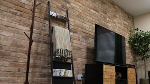 Uma parede de tijolos com um suporte de TV preto, uma escada e uma prateleira com revistas.