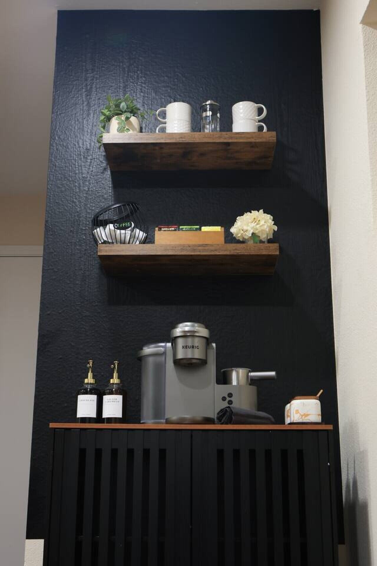 Een keuken met een koffiezetapparaat, twee flessen, een waterkoker en een kleine plant op een plank.
