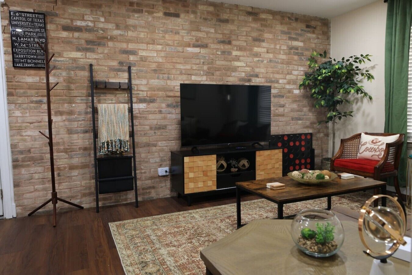 A living room with a brick wall, a flat-screen TV, a wooden coffee table, a sofa, a floor lamp, and a potted plant.