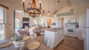 A modern kitchen with white cabinets, a central island, and a hanging light fixture. - Ocean View, Steps to Beach, 8-Person Hot Tub-HGTV Inspired Southern Charm (Avon)