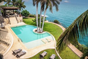 Un área de piscina con vista al océano, una estructura de techo de paja y una terraza ajardinada.