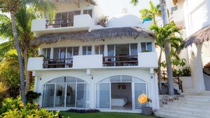 A multi-story building with balconies, large windows, and a thatched roof. - An exclusive beach house, perched on a cliff with panoramic ocean views. (Santa María Huatulco)