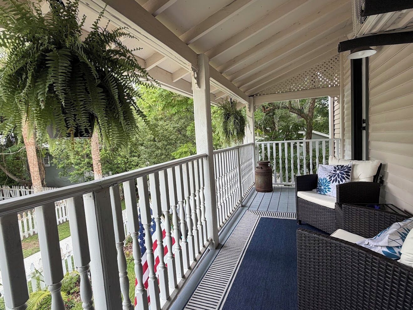 A covered porch with a railing, outdoor furniture, and a view of the surrounding greenery.