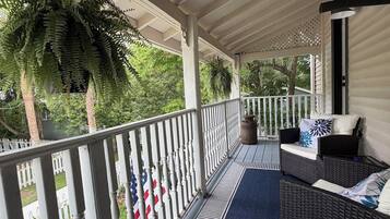 A covered porch with a railing, outdoor furniture, and a view of the surrounding greenery.
