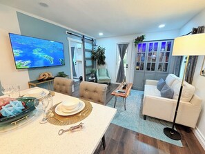 Uma sala de estar moderna com televisão de tela plana, uma área de jantar com mesa posta para quatro e um sofá.