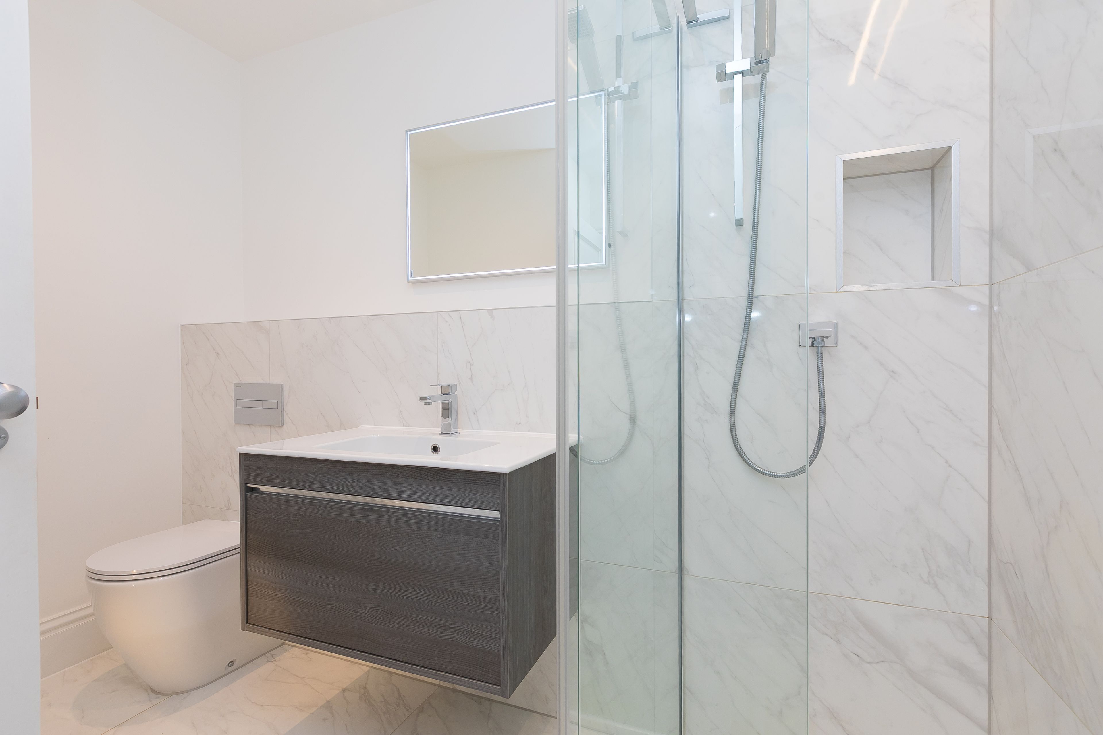 A modern bathroom with a glass shower enclosure, a white toilet, and a dark wooden vanity.
