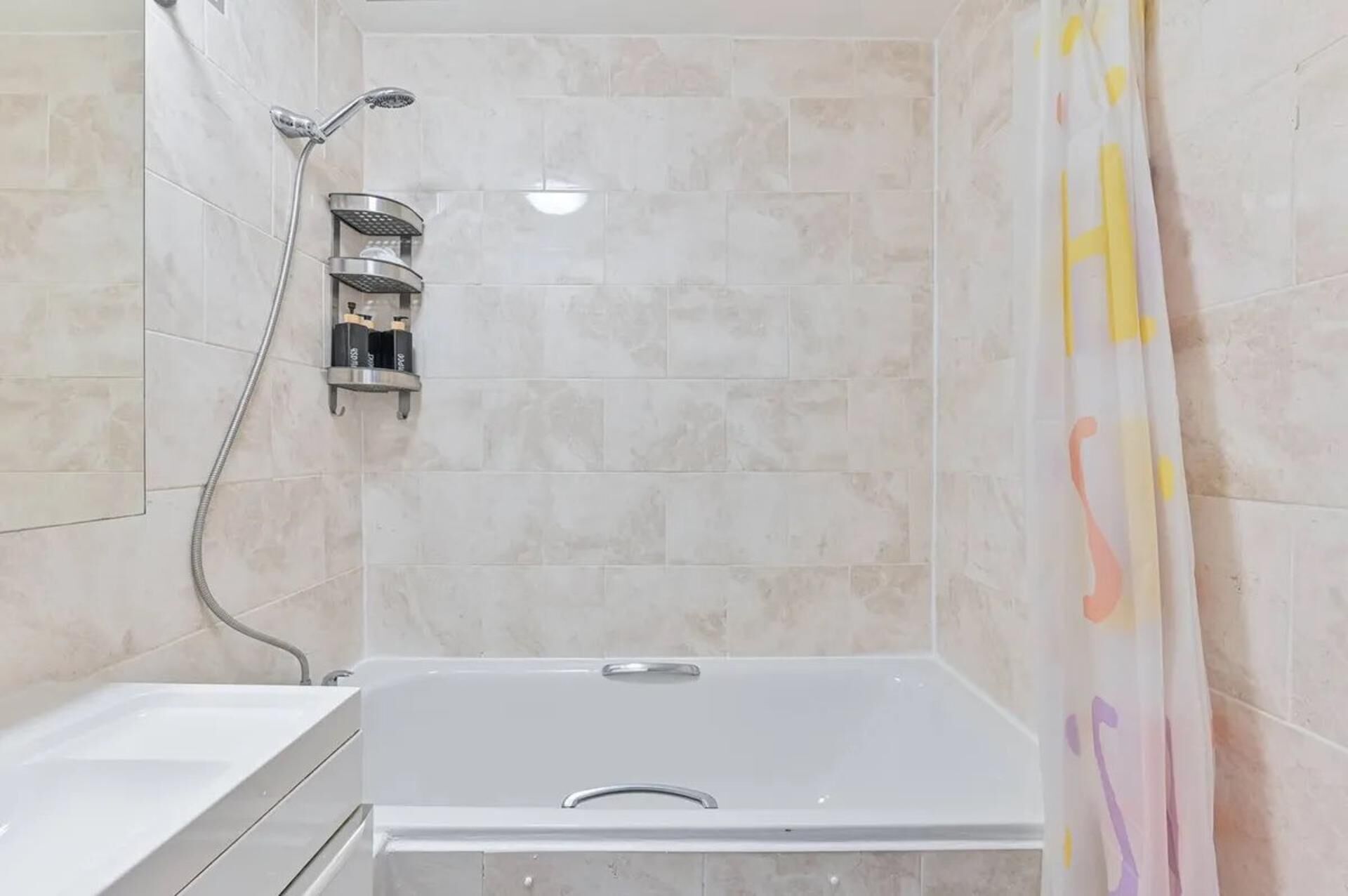 A bathroom with a bathtub, a shower with a handheld showerhead, and a wall-mounted soap dispenser.