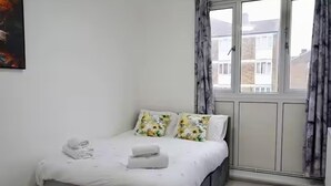A bedroom with a bed, pillows, a window with curtains, and a painting on the wall. - Cozy 2-bed Escape in Blackheath Smart Studio (London)