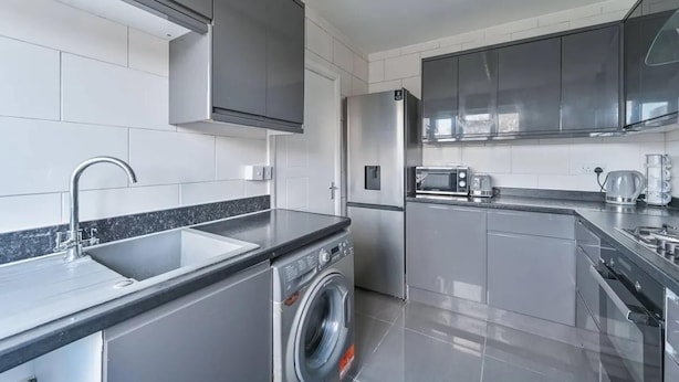 A modern kitchen with stainless steel appliances, a built-in washing machine, and a microwave. - Cozy 2-bed Escape in Blackheath Smart Studio (London)