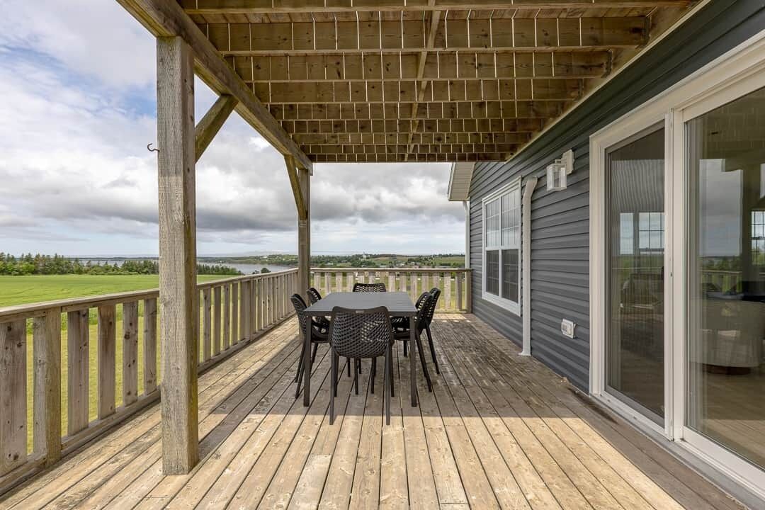 A covered deck with a table and chairs, overlooking a body of water and grassy area.