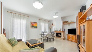 A living room with a sofa, a glass-top coffee table, a fireplace, a television, and a dining area with chairs and a table.