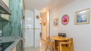 A dining area with a wooden table and chairs, a kitchen with a refrigerator and cabinets, and a hallway leading to another room.
