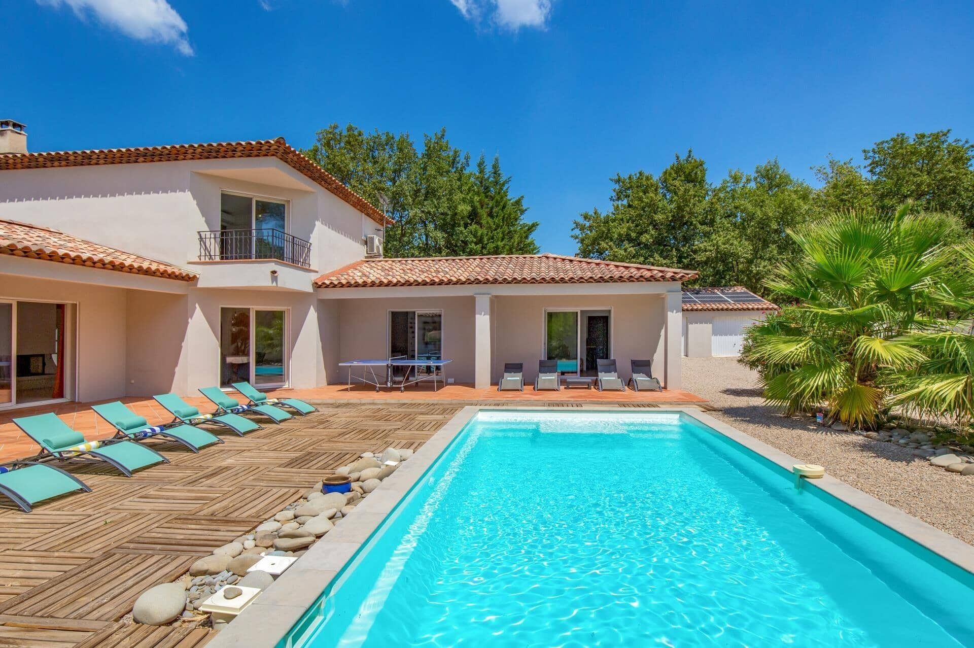 A two-story building with a swimming pool, lounge chairs, and a patio area.