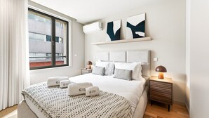 Une chambre d’hôtel moderne avec un grand lit, des tables de chevet, une fenêtre avec des rideaux et des œuvres d’art abstraites accrochées au mur.