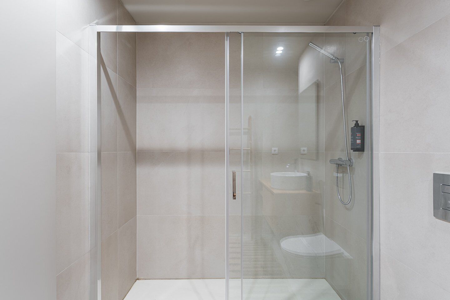 Een moderne douchecabine met een glazen deur, een handdouche en een wandmengkraan.