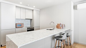 Une cuisine moderne avec des meubles blancs, un plan de travail en marbre, un four encastré, un évier et des tabourets de bar.