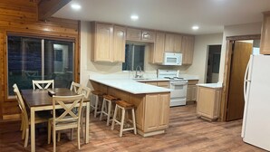 A kitchen with wooden cabinets, a white countertop, a dining table with chairs, and a refrigerator.