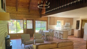 A spacious living area with a sofa, chairs, a dining table, and a kitchen with wooden cabinets and appliances.