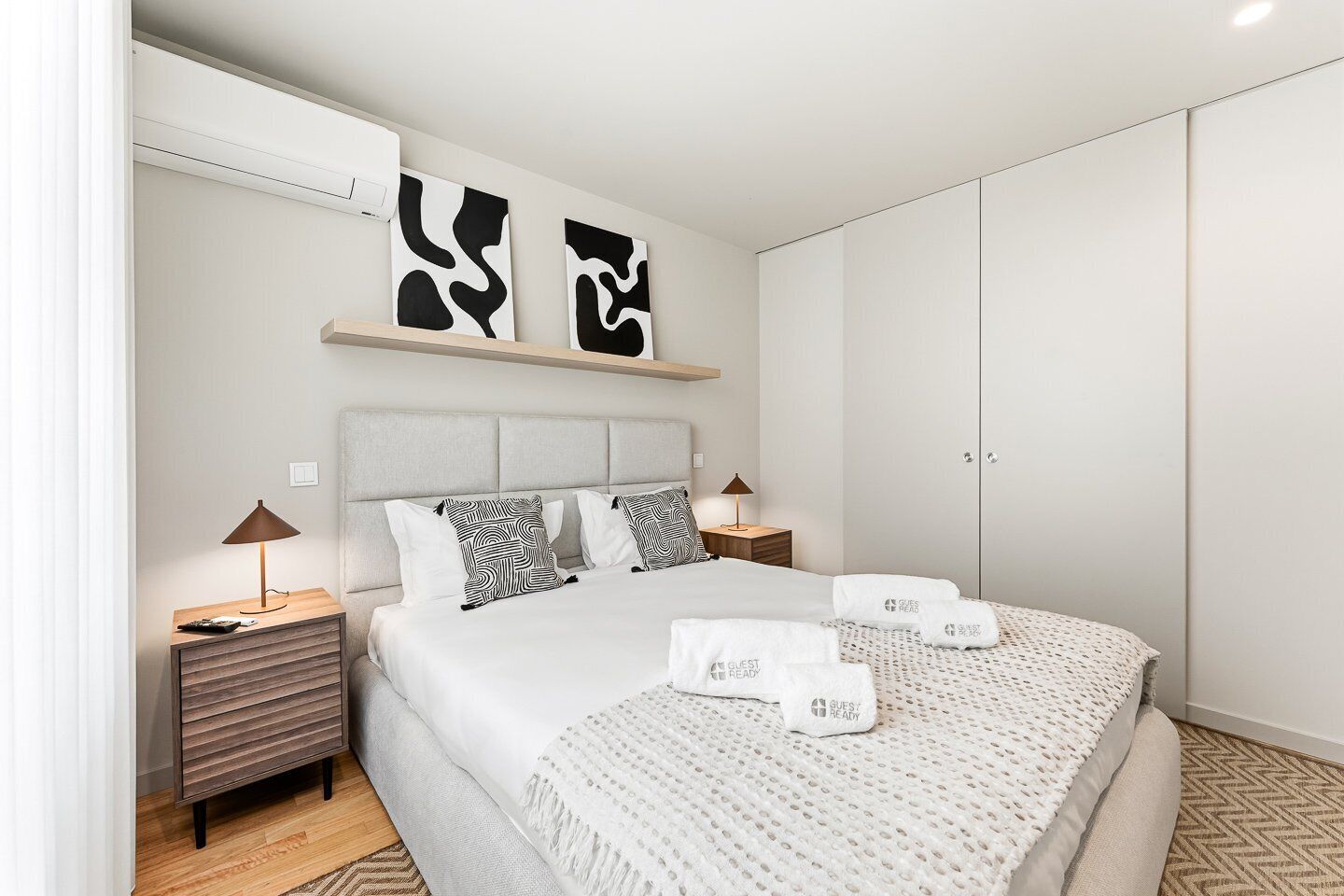 A modern hotel room with a bed, bedside tables, a wardrobe, and abstract wall art.